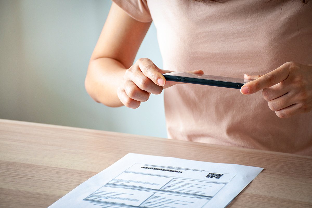 A person holding a smartphone over a printed document to scan it into a PDF